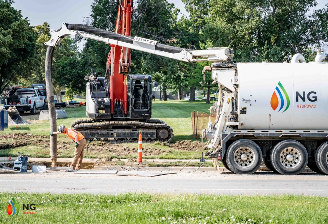 NG Companies hydrovac truck with employee guiding hydrovac, excavator in the background