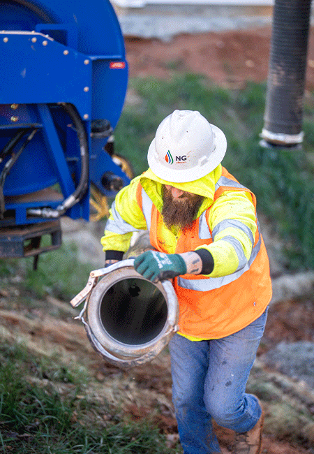 NG Companies employee holding hose walking up grass hill